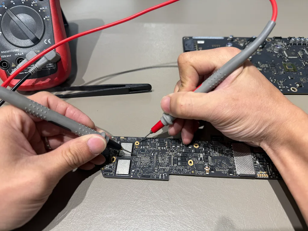Mac 主機板晶片級維修實況：技師使用三用電表 (Multimeter) 測量電路板供電數據，精準排查導致無法開機的硬體短路故障。