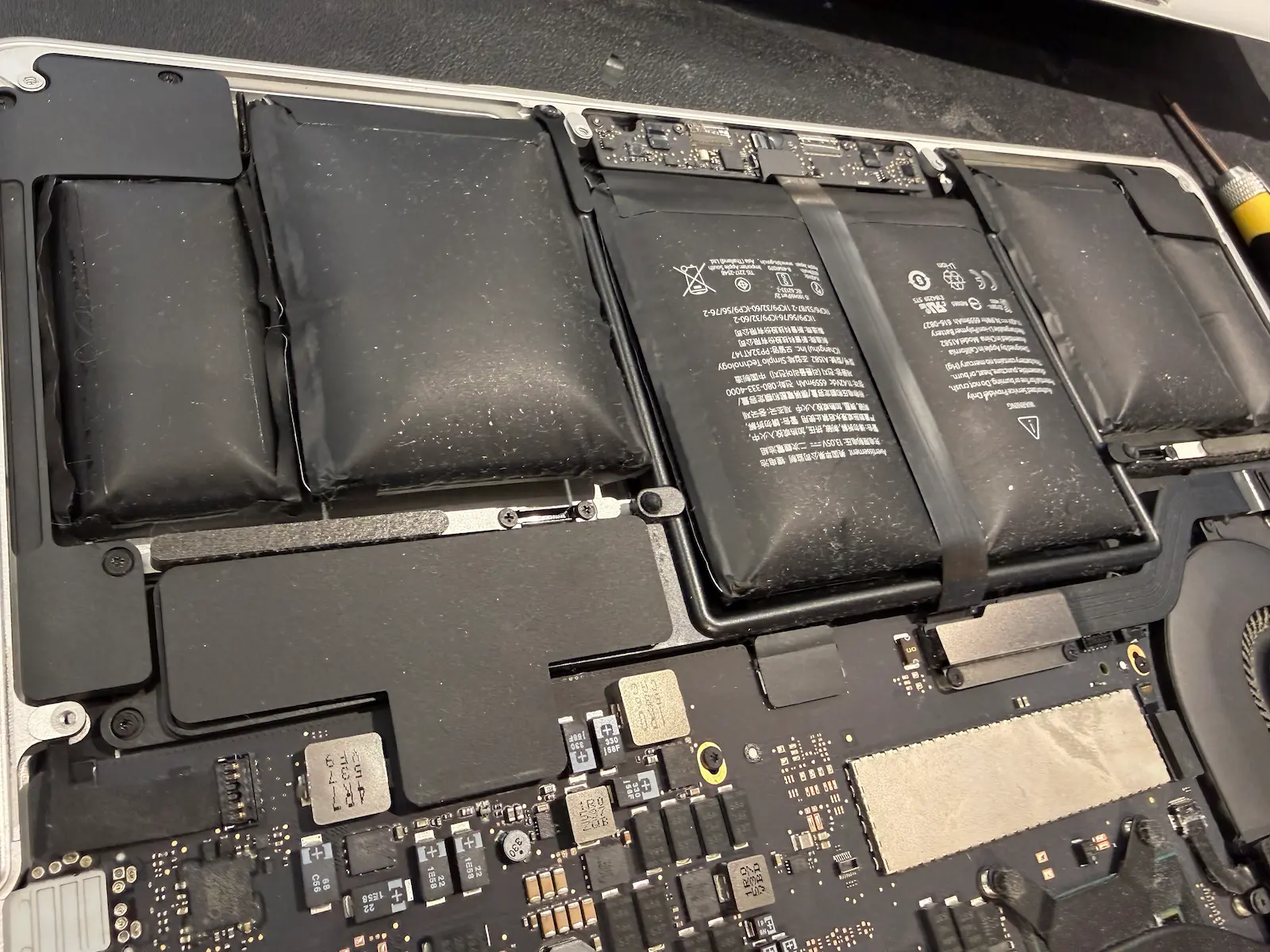 MacBook 鋰電池嚴重膨脹特寫,展示電池芯因化學反應產生氣體而大幅鼓起,已擠壓到觸控板與機身結構,屬於高風險安全隱患