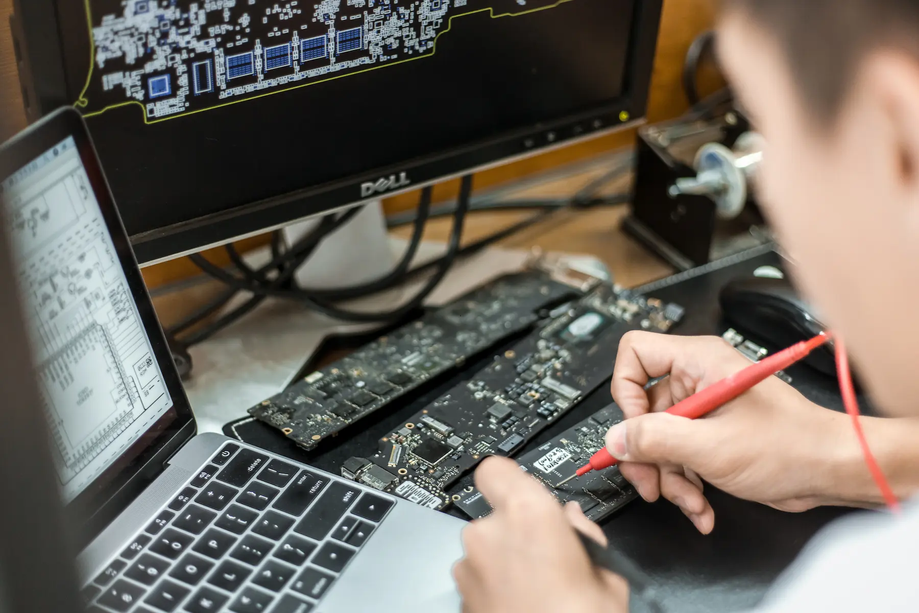 金日鑫 IRP 維修工程師正使用萬用電表,針對 MacBook 主機板進行主供電匯流排的精密電阻與電壓測量診斷