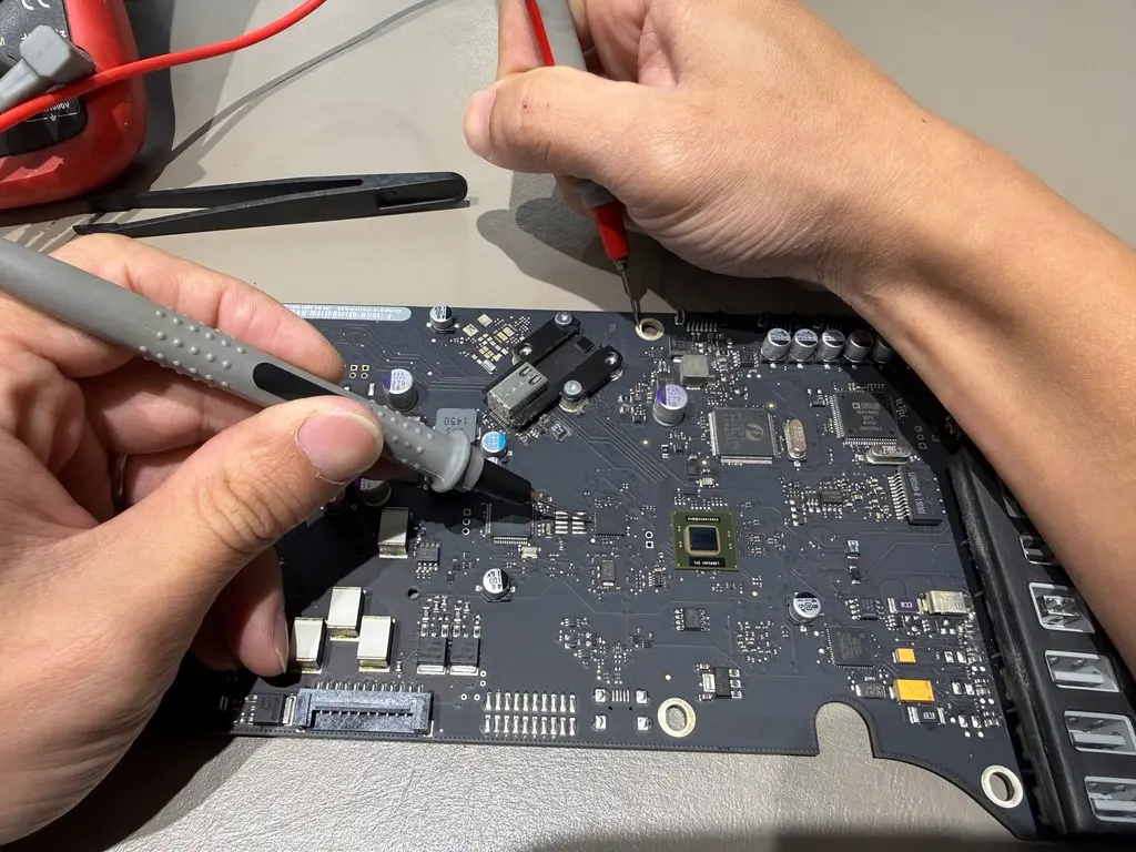 金日鑫蘋果電腦維修中心專業工程師,正使用萬用電表探針針對 MacBook 主機板進行精密的晶片級電路與板對板量測檢測